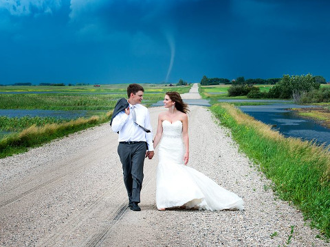 Photographer Captures Tornado in Couple's Wedding Pictures, a tornado touches in the distant background while a bride and groom walk down a country road in Saskatchewan, Canada, July 5, 2014 (Credit: Colleen Niska Photography via Facebook)