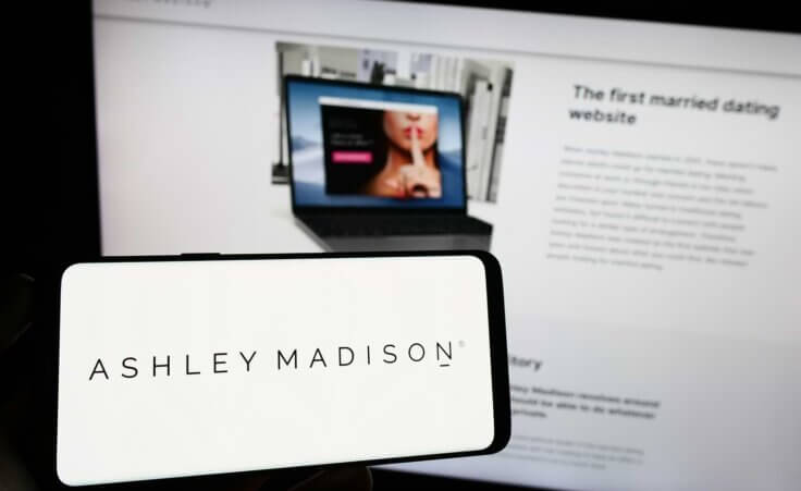 Person holding cellphone with logo of online dating company The Ashley Madison Agency on screen in front of webpage. By Timon/stock.adobe.com