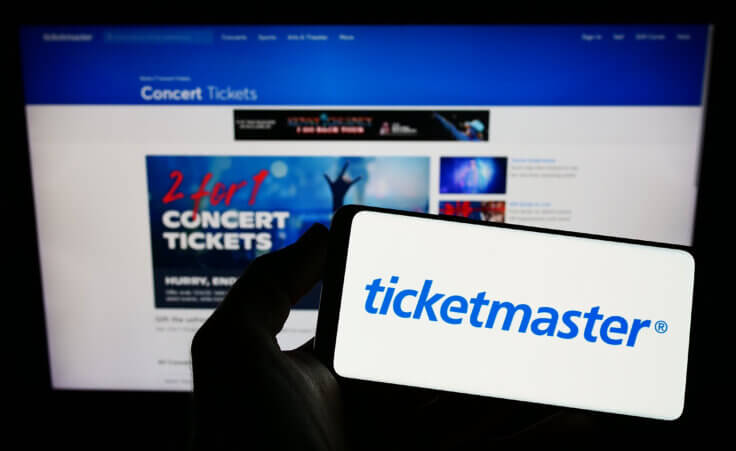 Person holding smartphone with logo of US company Ticketmaster Entertainment Inc. on screen in front of website. By Timon/stock.adobe.com