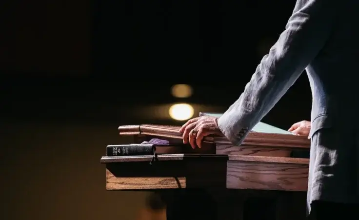 Pastor with hands on pulpit looking out at congregation. By Chris/stock.adobe.com