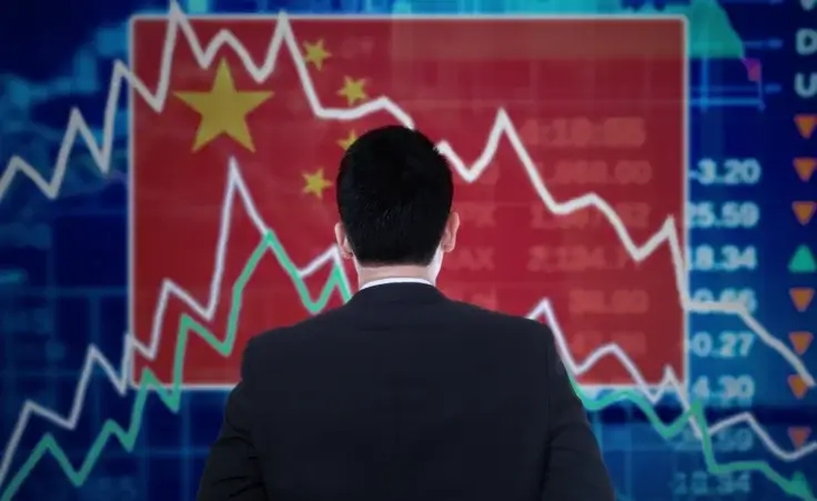 Man standing in front of stock market board with Chinese flag. By CreativaImages/stock.adobe.com. Economic collapse decline China.