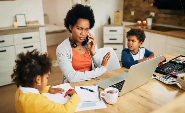 Mother with two kids talking on the phone while working on laptop at home to illustrate the surgeon general's new warning that parenting is "an urgent public health issue". By Drazen/stock.adobe.com