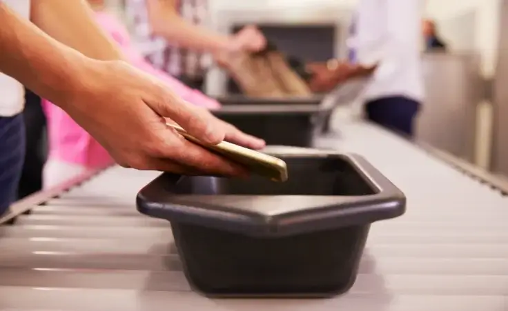 Man puts mobile phone into tray for airport security check. By Monkey Business/stock.adobe.com. Air travel