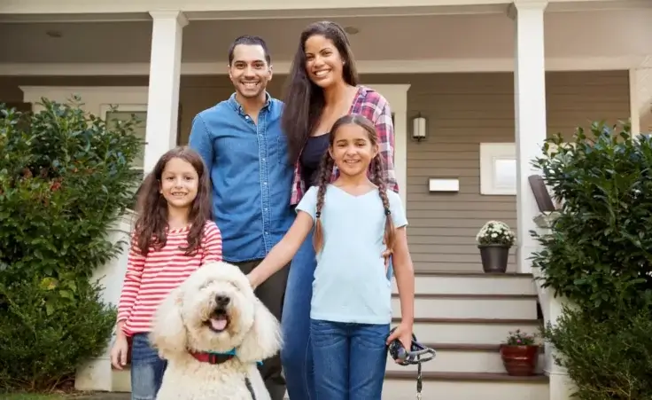 Portrait of a family standing in front of their house with pet dog to illustrate achieving the American Dream. By Monkey Business/stock.adobe.com