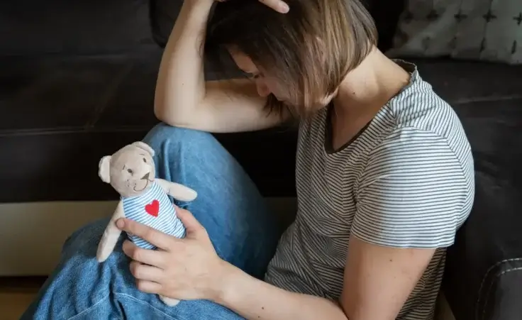 Woman grieving the loss of a child while holding a teddy bear toy to illustrate being disappointed by God. By anaumenko/stock.adobe.com