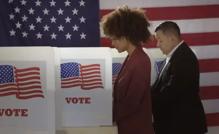 People in polling station, voting in a booth with US flag in background to illustrate Americans voting in the 2024 election. By vesperstock/stock.adobe.com