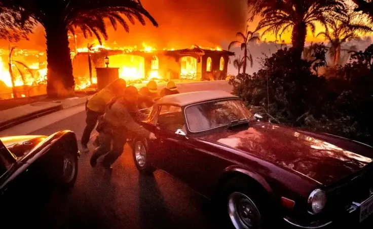 Firefighters and sheriff's deputies push a vintage car away from a burning home as the Mountain Fire burns in Camarillo, Calif., on Wednesday, Nov. 6, 2024. (AP Photo/Noah Berger)