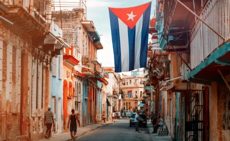 Cuban flag, people and aged buildings in Old Havana, Cuba. By kmiragaya/stock.adobe.com