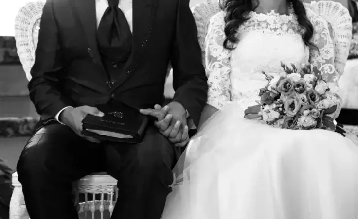 Grayscale shot of a bride and a groom holding hands during marriage ceremony in grayscale By Vlad Negru/Wirestock/stock.adobe.com