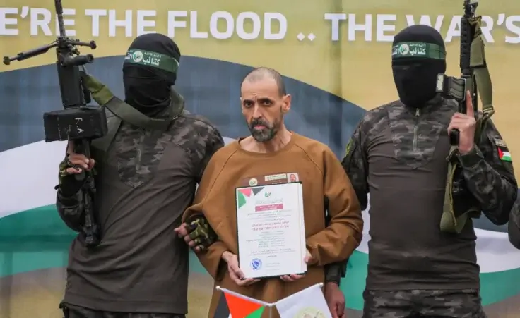 Israeli captive, Eli Sharabi, who has been held hostage by Hamas in Gaza since October 7, 2023, stands on a stage escorted by Hamas fighters before being handed over to the Red Cross in Deir al-Balah, central Gaza Strip, Saturday Feb. 8, 2025. (AP Photo/Abdel Kareem Hana) Gaza hostages