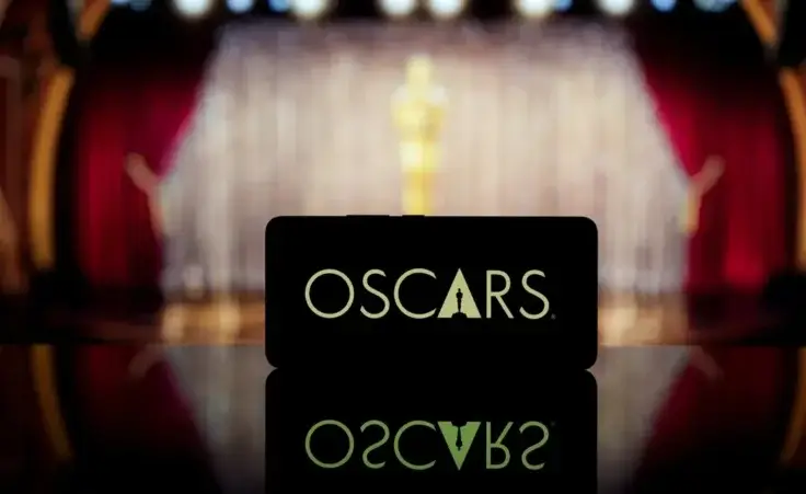 A smartphone displaying the Oscars logo against a blurred awards ceremony background. By Rokas/stock.adobe.com